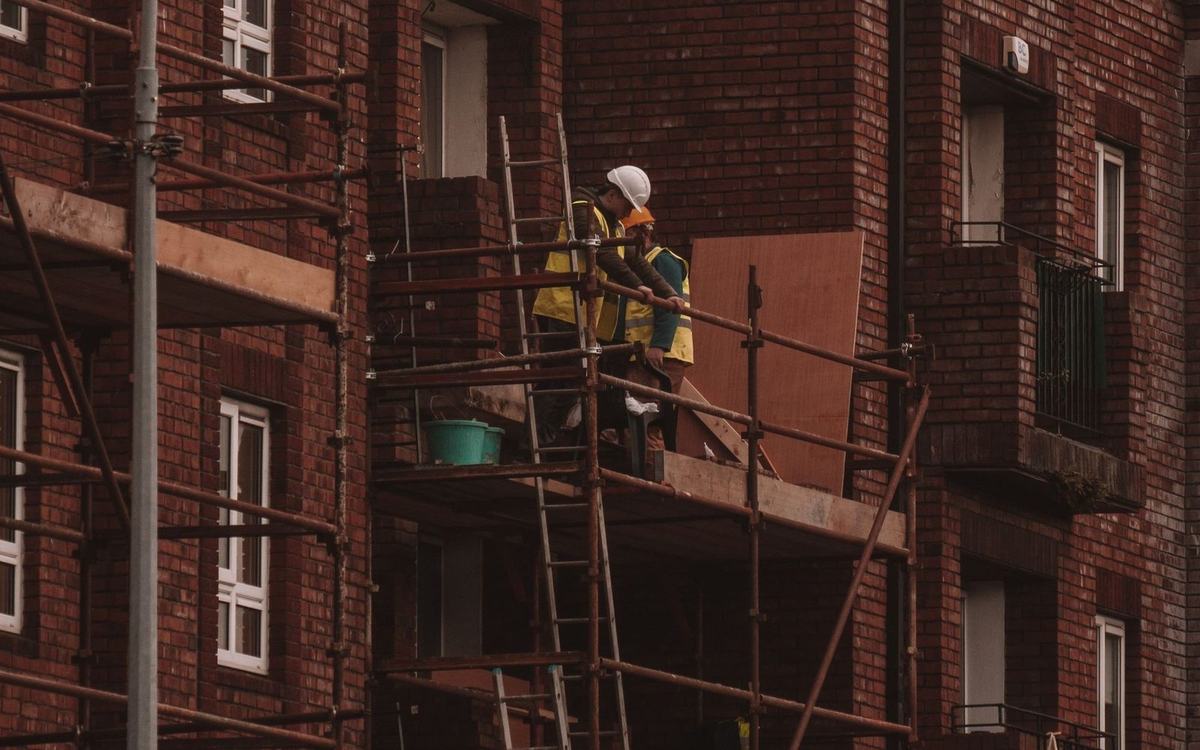 Scaffolders working on a platform against a brick house